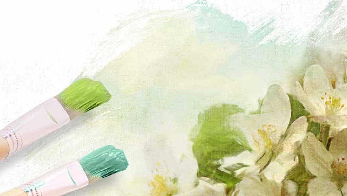 two artist brushes with green and blue paint resting on a work in progress of white flowers with green leaves