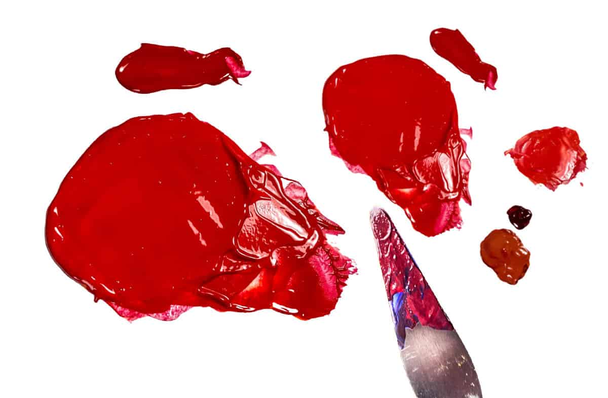 Shades of red paint and a palette knife covered in red paint on a white background.