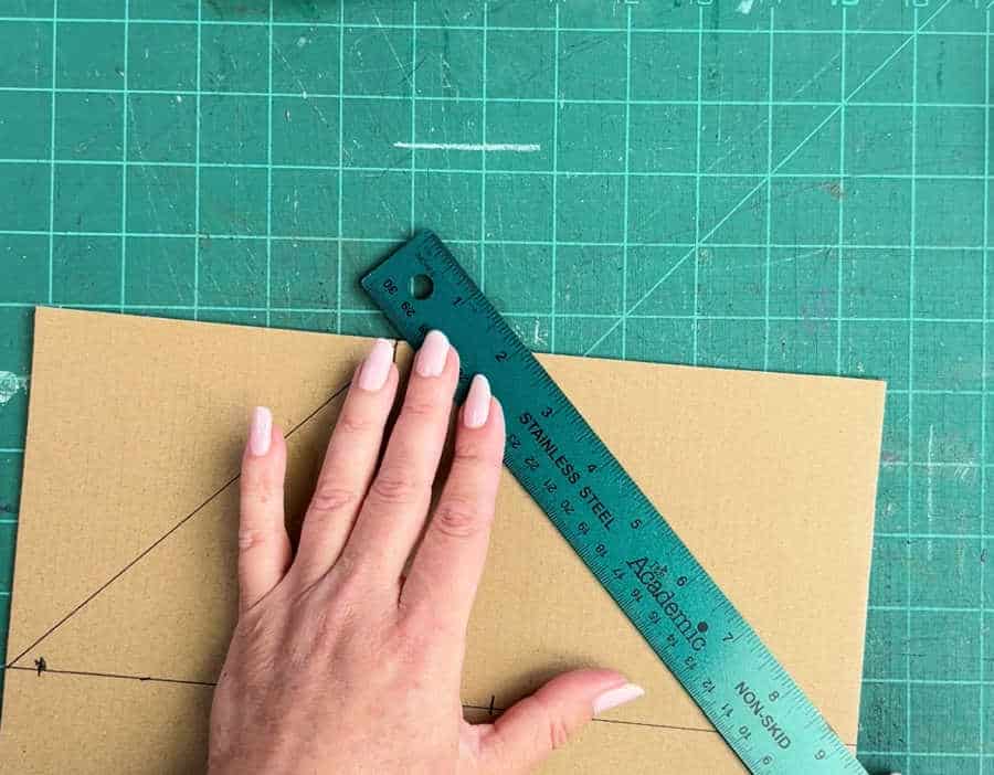 A picture showing how to draw the top line on cardboard for a corner protector using a ruler and pen.