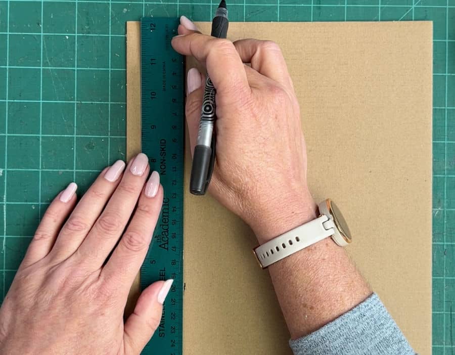 A picture showing how to draw the bottom line on cardboard for a corner protector using a ruler and pen.