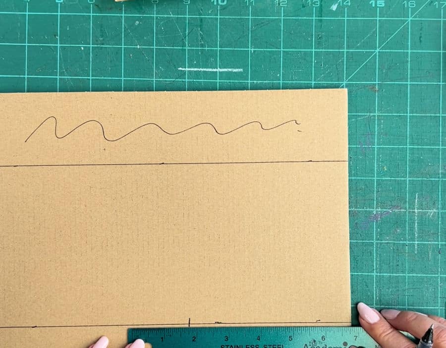 A picture showing how to how to measure 1.75 inches from the previous 5 inch mark on cardboard for a corner protector using a ruler and pen.