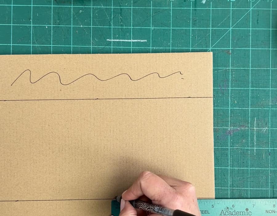 A picture showing how to how to measure in 5 inches from the side on cardboard for a corner protector using a ruler and pen.