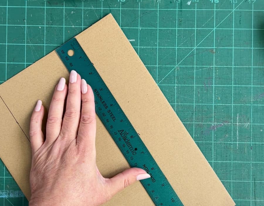 A picture showing how to draw the top line on cardboard for a corner protector using a ruler and pen.