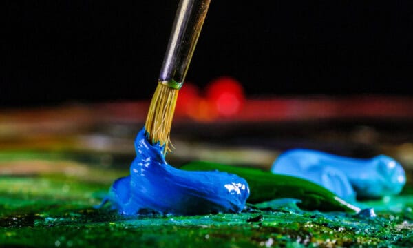 Closeup of an artist brush swirling blue oil paint on a palette.