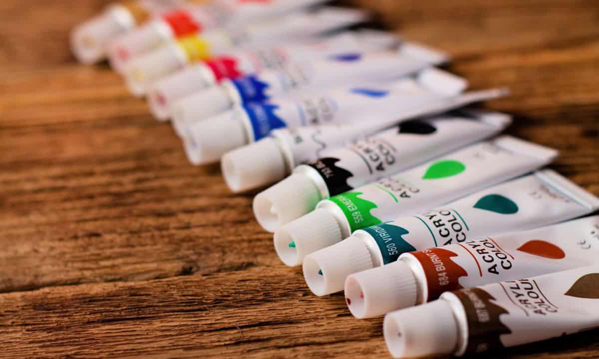 Artist paint tubes laid out in a row on a wooden table.