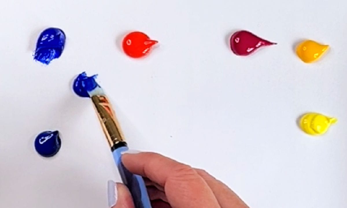An artist holding a paintbrush mixing various colours of paint.