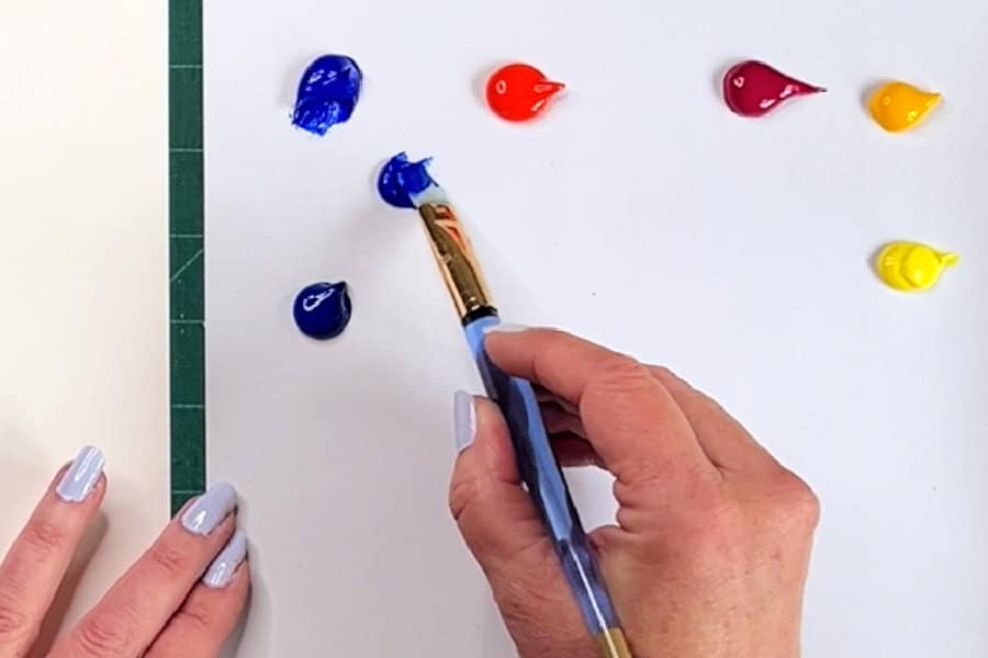 An artist holding a paintbrush mixing various colours of paint.