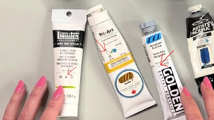 Four tubes of various brands and colours of acrylic paint with red arrows pointing to squares showing if they are transparent or opaque.