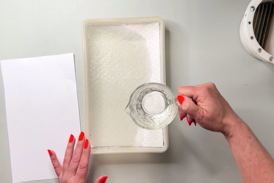 An artist pouring water from a jug over paper towels in a diy wet palette.