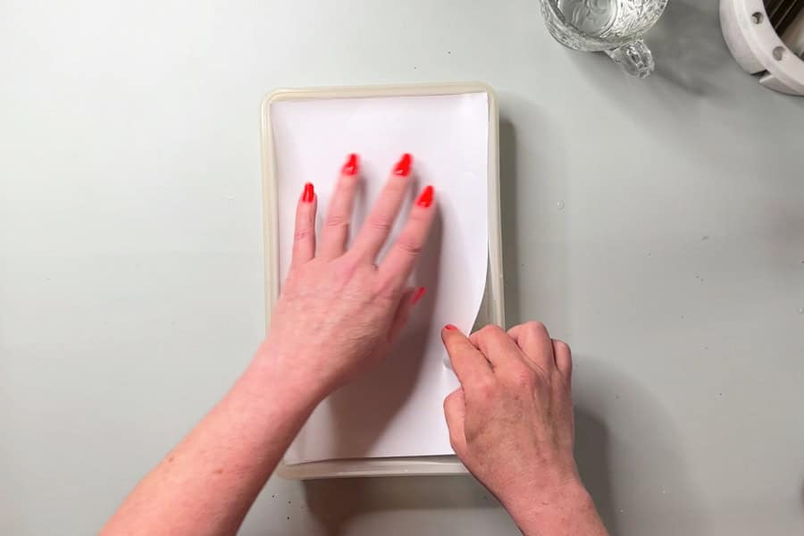 An artist fitting palette paper into a plastic container.