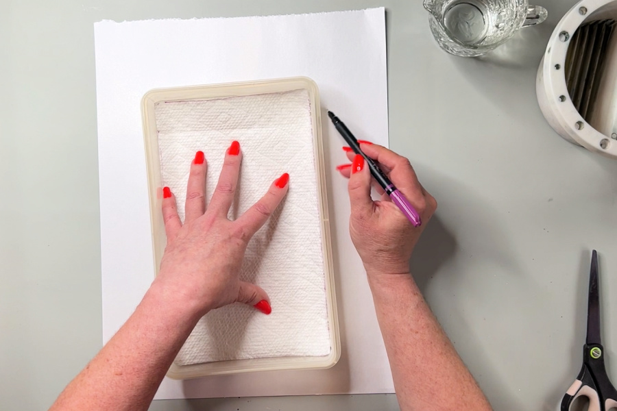 An artist using a plastic container as a template to measure palette paper to insert into a diy wet palette.