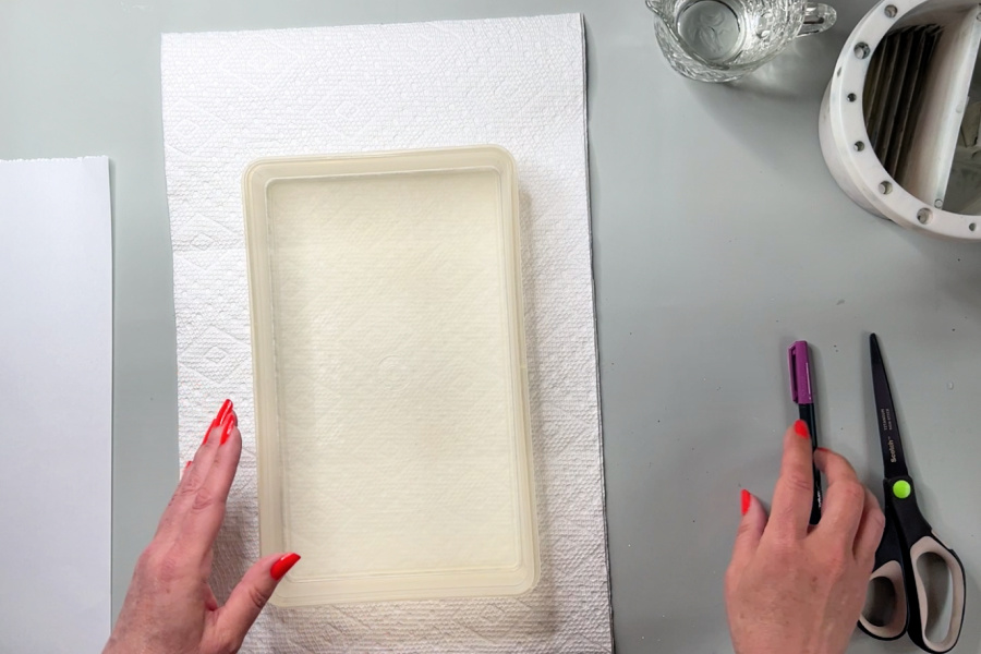 An artist using an empty plastic container to measure paper towels for placement into a diy wet palette.