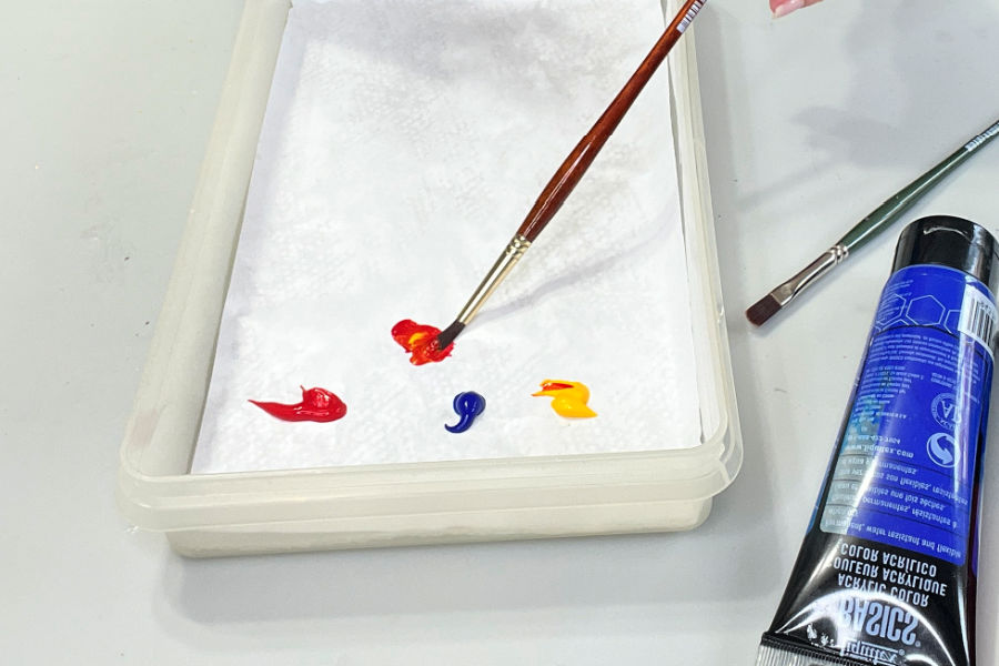 Red, blue, and yellow paint in a diy wet palette with artist brushes and paint tubes.